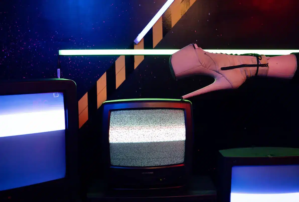 Set cinematografico con estetica anni '70-'80 reinterpretata in chiave sci-fi, illuminato da luci neon e grafiche pubbli