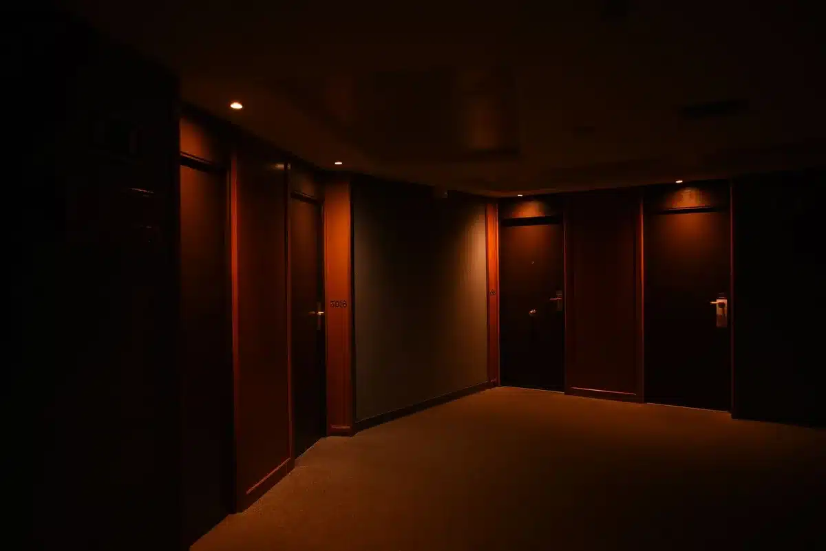 Corridoio di hotel vuoto e isolato con porte chiuse e illuminazione cupa