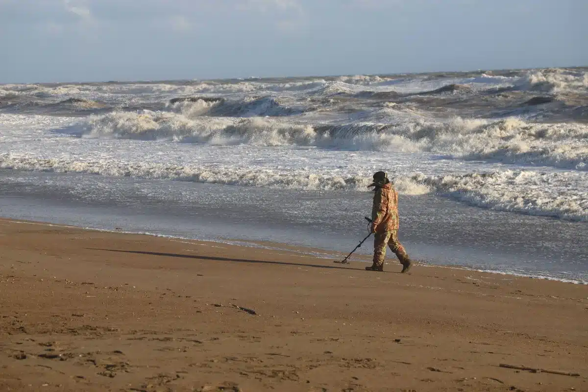 Persona che utilizza un metal detector su una spiaggia sabbiosa cercando tesori