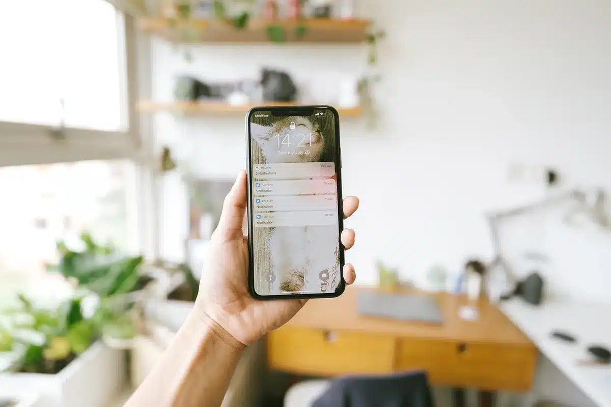 Mani anonime che scrivono su uno smartphone con notifiche sfocate, in un ufficio luminoso