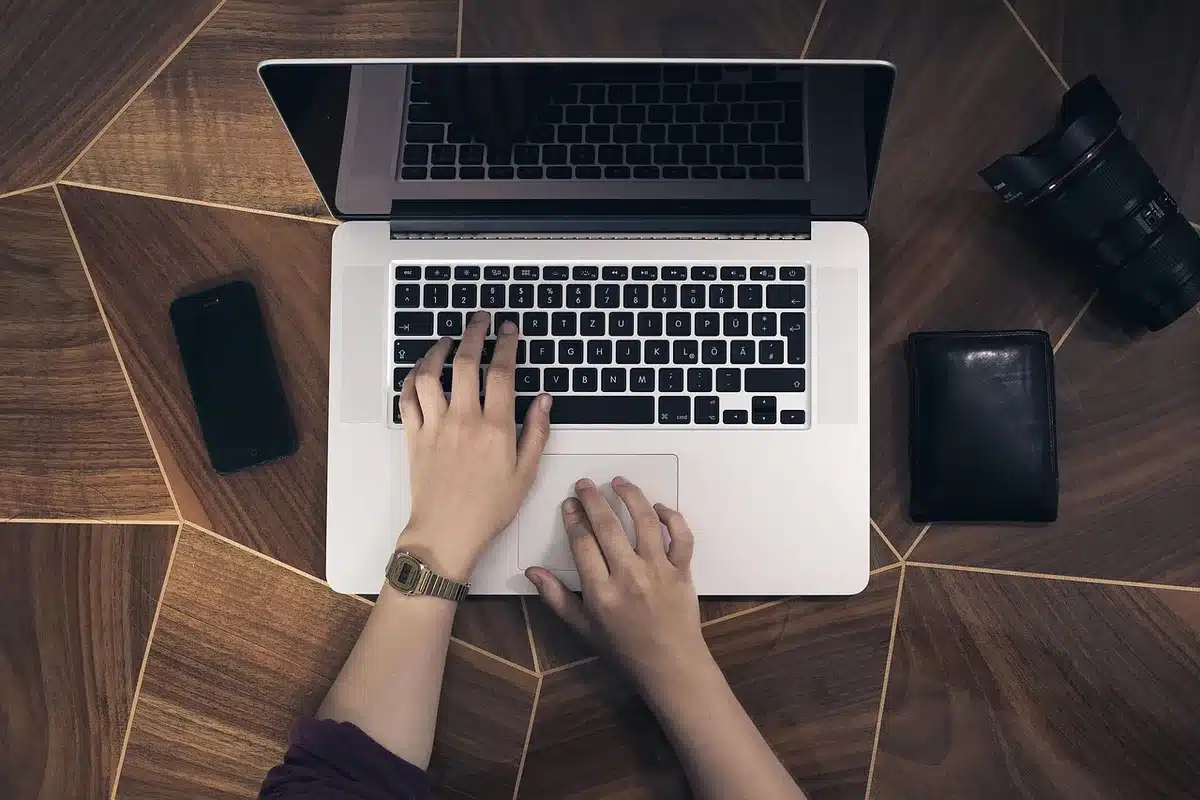Persona anonima con laptop e smartphone al tavolo di un bar vicino a un router Wi‑Fi pubblico